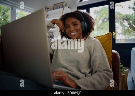 Porträt von fröhlichen jungen schwarzen Frau, die Audio in Kopfhörer, während Sie Videos auf dem Laptop zu Hause ansehen Stockfoto