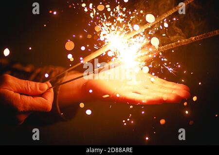 Funken und Licht von Wunderkerzen im Dunkeln auf der Handfläche einer Person. Weihnachtszauber, Silvester, festlicher Hintergrund. Leerzeichen für Text Stockfoto