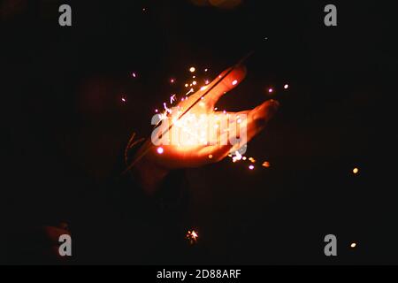 Funken und Licht von Wunderkerzen im Dunkeln auf der Handfläche einer Person. Weihnachtszauber, Silvester, festlicher Hintergrund. Leerzeichen für Text Stockfoto