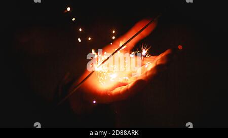 Funken und Licht von Wunderkerzen im Dunkeln auf der Handfläche einer Person. Weihnachtszauber, Silvester, festlicher Hintergrund. Leerzeichen für Text Stockfoto