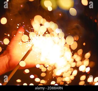 Funken und Licht von Wunderkerzen im Dunkeln auf der Handfläche einer Person. Weihnachtszauber, Silvester, festlicher Hintergrund. Leerzeichen für Text Stockfoto