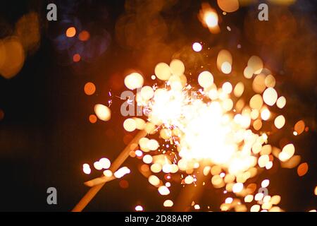 Funken und Licht von Wunderkerzen im Dunkeln mit hellem Gelb und Orange Bokeh und Rauch. Festliche Feuer Textur, Hintergrund für Neujahr und Weihnachten Stockfoto