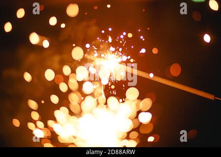 Funken und Licht von Wunderkerzen im Dunkeln mit hellem Gelb und Orange Bokeh und Rauch. Festliche Feuer Textur, Hintergrund für Neujahr und Weihnachten Stockfoto