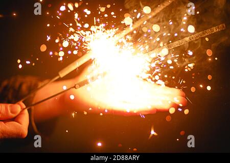 Funken und Licht von Wunderkerzen im Dunkeln auf der Handfläche einer Person. Weihnachtszauber, Silvester, festlicher Hintergrund. Leerzeichen für Text Stockfoto