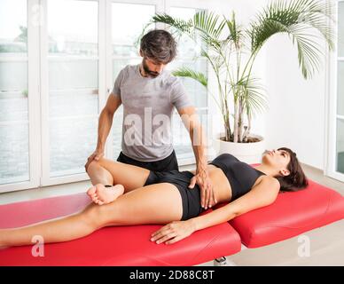 Osteopath, der eine Hüftanalyse in seiner Klinik macht und die überprüft Beweglichkeit und Funktion des Gelenkes bei einer jungen Frau Patient auf einem Tisch Stockfoto