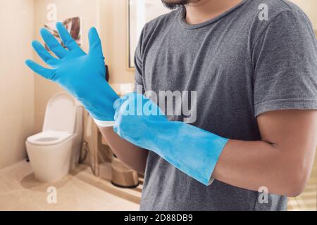 Bangkok / Thailand - September 20 2020 : der Mann in einem grauen Hemd mit blauen Gummihandschuhen vor dem Toilettenwaschen. Stockfoto