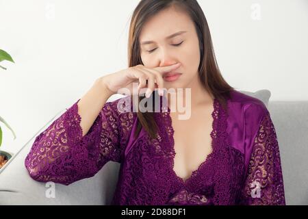 Asiatische Frauen in Satin lila Nachthemd Gefühl unwohl und Sinus vor einem grauen Hintergrund. Stauballergien. Grippe. Menschen erkältet und allergisch. Stockfoto