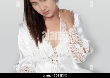 Schulterschmerzen oder verlockte Schulter bei einer Frau, Ache eingeklemmt Nerven in den Hals oder die Schulter, Lady trägt weißen Nachthemd & Langarm Satin Robe wit Stockfoto