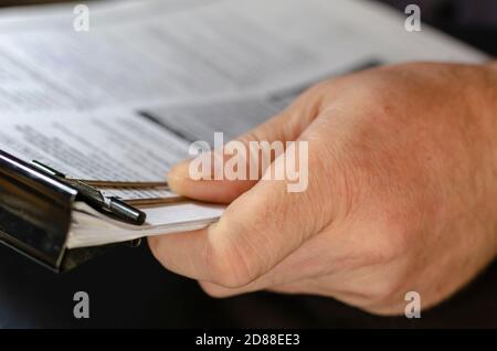 Nahaufnahme von männlichen Händen, die Papierblätter mit schwarzer Metallklammer halten. Die Blätter sind mit Text gefüllt. Spuren von blauer Tinte auf dem Finger des Menschen. Selektiver Fokus. Stockfoto