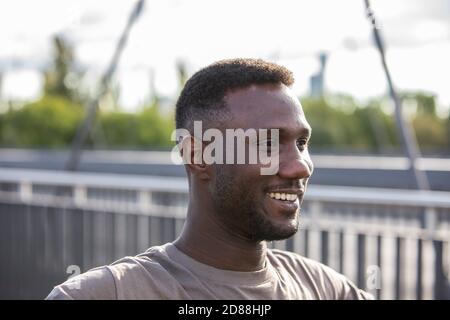 Junger afrikanischer Ethnie Mann lächelt im Freien. Seitenansicht. Hochformat. Nahaufnahme. Über den Schultern. Stockfoto