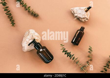 Natürliche Bio-Kosmetik. Schwarze Flaschen aus Glas ohne Marken auf Natursteinen und Eukalyptusblättern. Home Spa-Konzept. Draufsicht, flach liegend. Stockfoto