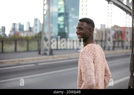 Schöner Mann lächelt auf der Straße mit dem Kopf gedreht. Rückansicht. Seitenansicht. Mittlere Aufnahme. Stockfoto