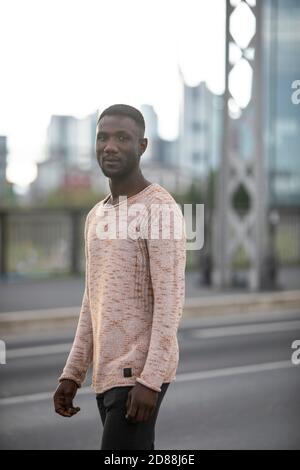 Junger schwarzer Mann, der mit dem Kopf vor der Kamera auf dem Hintergrund der Stadt läuft. Dreiviertel Länge. Fokus auf Vordergrund. Stockfoto