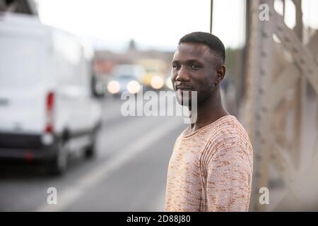 Mann auf der Straße mit Autos im Hintergrund. Geringe Schärfentiefe. Fokus auf Vordergrund. Seitenansicht. Mittlere Aufnahme. Stockfoto