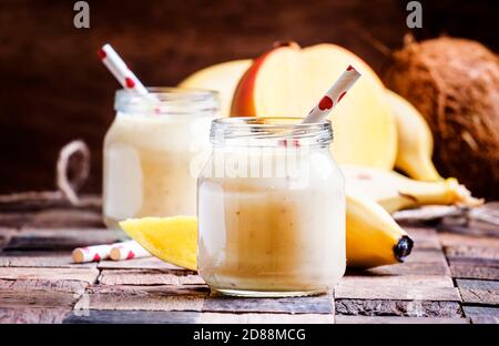 Banana Mango Smoothie mit Kokosnuss in einem Glas, vintage Holzhintergrund, selektiver Fokus Stockfoto