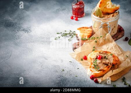 Köstliche Pastete Hühnerleber und Fleisch auf gegrilltem Toast mit Preiselbeeren und Thymian, grauer Küchentisch Hintergrund, Platz für Text, selektiver Fokus Stockfoto