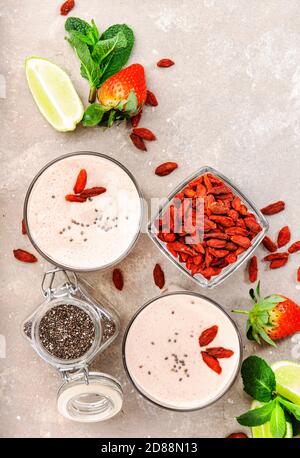 Gesundes Mixgetränk. Bio-veganer Smoothie ohne Milchprodukte mit Erdbeer- und Goji-Beeren, Chiasamen und Limette. Grauer Hintergrund mit Kopierbereich. Oben vi Stockfoto