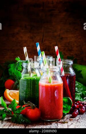 Mix aus gesunden Obst- und Gemüsesäften in kleinen Flaschen mit farbig gestreiften Trinkhalmen, altem Holzhintergrund, selektiver Fokus Stockfoto