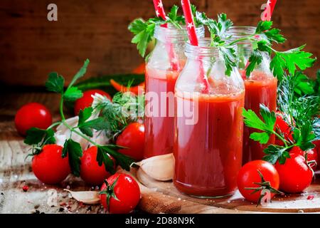 Würziger Tomatensaft in kleinen Flaschen mit Strohhalmen, Kirschtomaten, Petersilie, Dill, Knoblauch, Gewürzen und Salz, selektiver Fokus Stockfoto