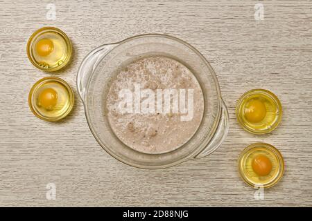 Eine Schüssel fermentierte verdünnte Hefe vier runde Behälter in jedem der zerbrochenen Eier. Stockfoto