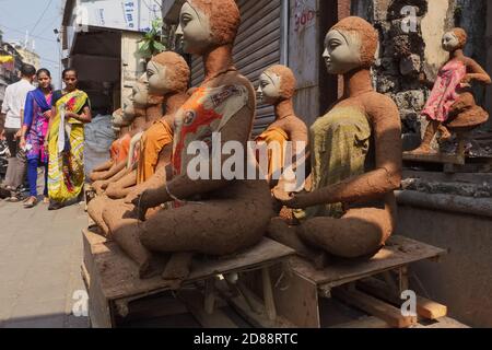 Zwei Frauen passieren frisch gemachte Tonfiguren der Hindu-Göttin Durga, die sich zum Trocknen in der Sonne aufmachen; Gulalwadi-Gegend, Mumbai, Indien Stockfoto