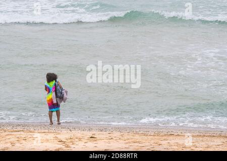 Ein Urlauber, der in einem bunten Kleid am Fistral Beach in Newquay in Cornwall auf einem Aufenthaltstag ist. Stockfoto