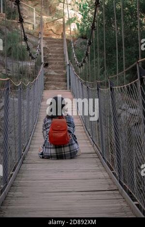 Backpacker Mädchen auf einer Hängebrücke in Chulilla sitzen, erkunden und genießen Sie die Natur. Rucksackreisen. Wanderaktivitäten. Aktivitäten im Freien. Stockfoto