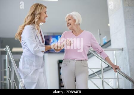 Doktor in einem Laborkittel, der ihre Patientin unterstützt und lächelt Stockfoto