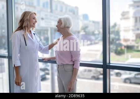 Arzt legt ihre Hand auf die Schulter des Patienten und zeigt Unterstützung Stockfoto