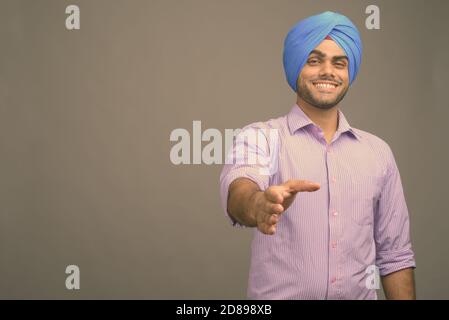 Junger gutaussehender indischer Geschäftsmann trägt Turban vor grauem Hintergrund Stockfoto