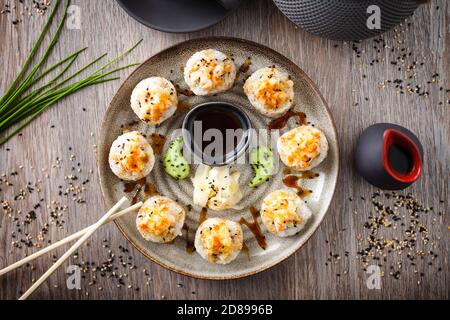 Gebackene Sushi-Maki-Brötchen mit Garnelen und Krabben auf einem Teller mit Essstäbchen, Sojasauce, Wasabi und Ingwer. Japanische traditionelle Fischgerichte aus der Nähe serviert Stockfoto