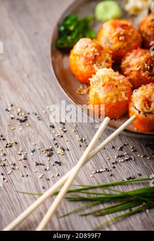 Gebackene Sushi-Maki-Brötchen mit Lachs, Krabben, Gurken, Avocado, fliegendem Fischrogen und würziger Sauce auf einem Teller mit Essstäbchen, Sojasauce, Wasabi und Ingwer Stockfoto