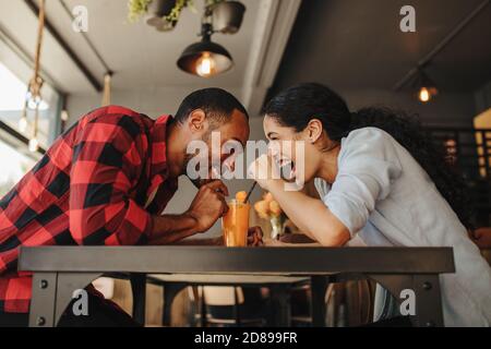 Glücklicher Mann und Frau, die Saft aus einem Glas in einem Café trinken. Schönes Paar genießen zusammen auf einem Date. Stockfoto