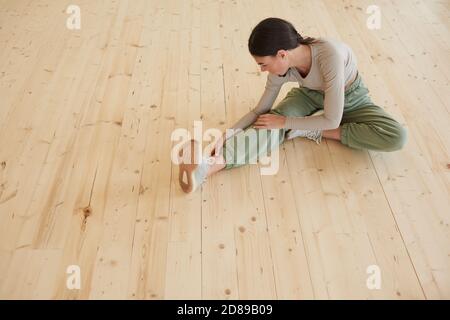 Junge schlanke Frau sitzt auf dem Boden und streckt sie Beine während des Trainings im Fitnessstudio Stockfoto