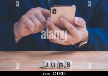 Closeup Holzblock schriftliche Jobs Suche auf dem Tisch gegen bussinessman mit Smartphone, um neue Jobs und Anwendung zu finden. Beschäftigungskonzept. Stockfoto