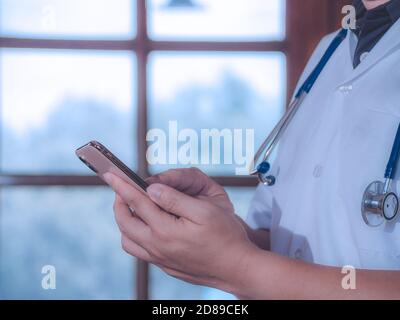 Männlicher Arzt mit Smartphone finden Informationen und hält Stethoskop im Krankenhaus. Gesundheitswesen und Medizin Konzept. Stockfoto