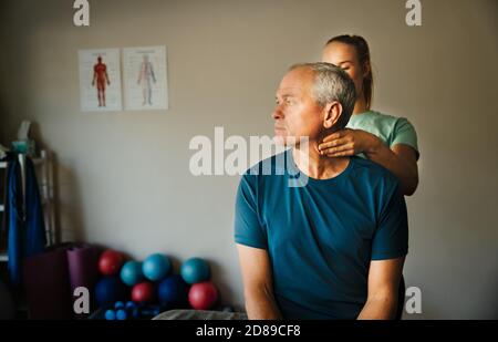 Der männliche Patient verdrehte seinen Hals, während der weibliche Physiotherapeut im Reha-Raum die Nerven des Halses einkniff massiert. Stockfoto