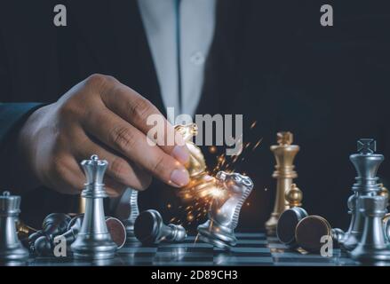 Hand Geschäftsmann bewegen den goldenen Ritter Schach kämpfen silbernen Ritter mit Feuer Funken Schach auf dem Schachbrett erfolgreich im Wettbewerb. Manag Stockfoto