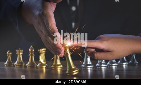 Hand des Geschäftsmannes hält Goldkönig Schach vom Fallen über den Angriff des Gegners mit Feuer Funken Licht. Geschäftspartner oder Zusammenarbeit. Unternehmen Stockfoto