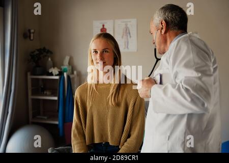Männlicher Arzt mit Stethoskop, um Herzschlag von weiblichen Patienten auf dem Bett im professionellen Büro zu hören. Stockfoto