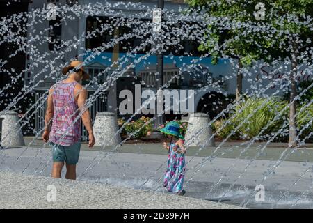 Ein junges Mädchen und ihr Vater spielen zusammen in der Hoher Springbrunnen im Georgetown Waterfront Park Stockfoto