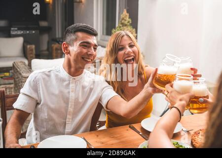 Gemischtes Rennpaar, das Pizza isst und laut lacht. Freunde essen und trinken zusammen Stockfoto