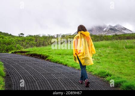 Skaftafell, Island grüne Sommerlandschaft und Frau in gelben Poncho Wandern Wandern auf nassen Pfad Wanderweg Wanderweg und bewölkten Himmel mit Bergen Stockfoto