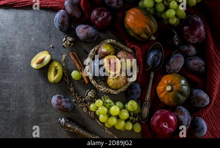 Stillleben mit frischem Obst und Gemüse auf dunkelgrauem Tisch. Draufsicht Foto von Edelstein Squashes, Trauben, Pflaumen, rot strukturierte Küchentuch. Stockfoto