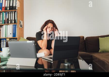 Gestresste Geschäftsfrau, die von zu Hause aus auf einem Laptop arbeitet und besorgt, müde und überwältigt aussieht Stockfoto
