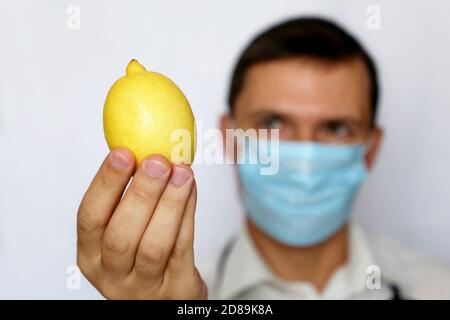 Influenza-Prävention, Mann in medizinischer Maske mit Zitrone in der Hand. Quelle von Vitamin C, Stärkung der Immunität während der Erkältungs- und Grippesaison Stockfoto