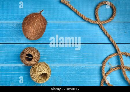 Reife Kokosnuss, zwei Sceins aus Jute Garn oder Faden und ein Seil auf blauem Holzhintergrund oder Desktop. Nahaufnahme, Kopierbereich Stockfoto