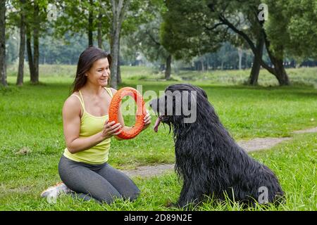 Lächelnde Frau spielt mit Hund auf Gras im Park. Stockfoto