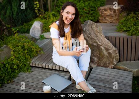 Freiberufliche junge Frau kommuniziert mit Kunden am Telefon, während Sitzen in einem grünen Park Stockfoto