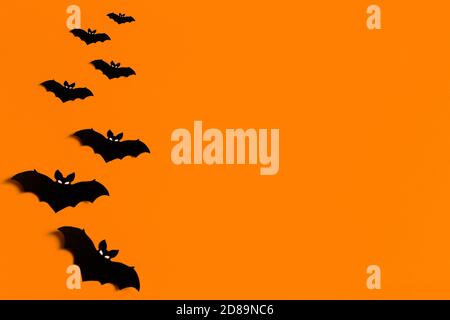 Oranger Hintergrund mit einer Schar von schwarzen Papier Fledermäuse für Halloween, schwarze Papier Fledermaus Silhouetten auf einem orangen Hintergrund, Halloween-Konzept, Copyspace Stockfoto